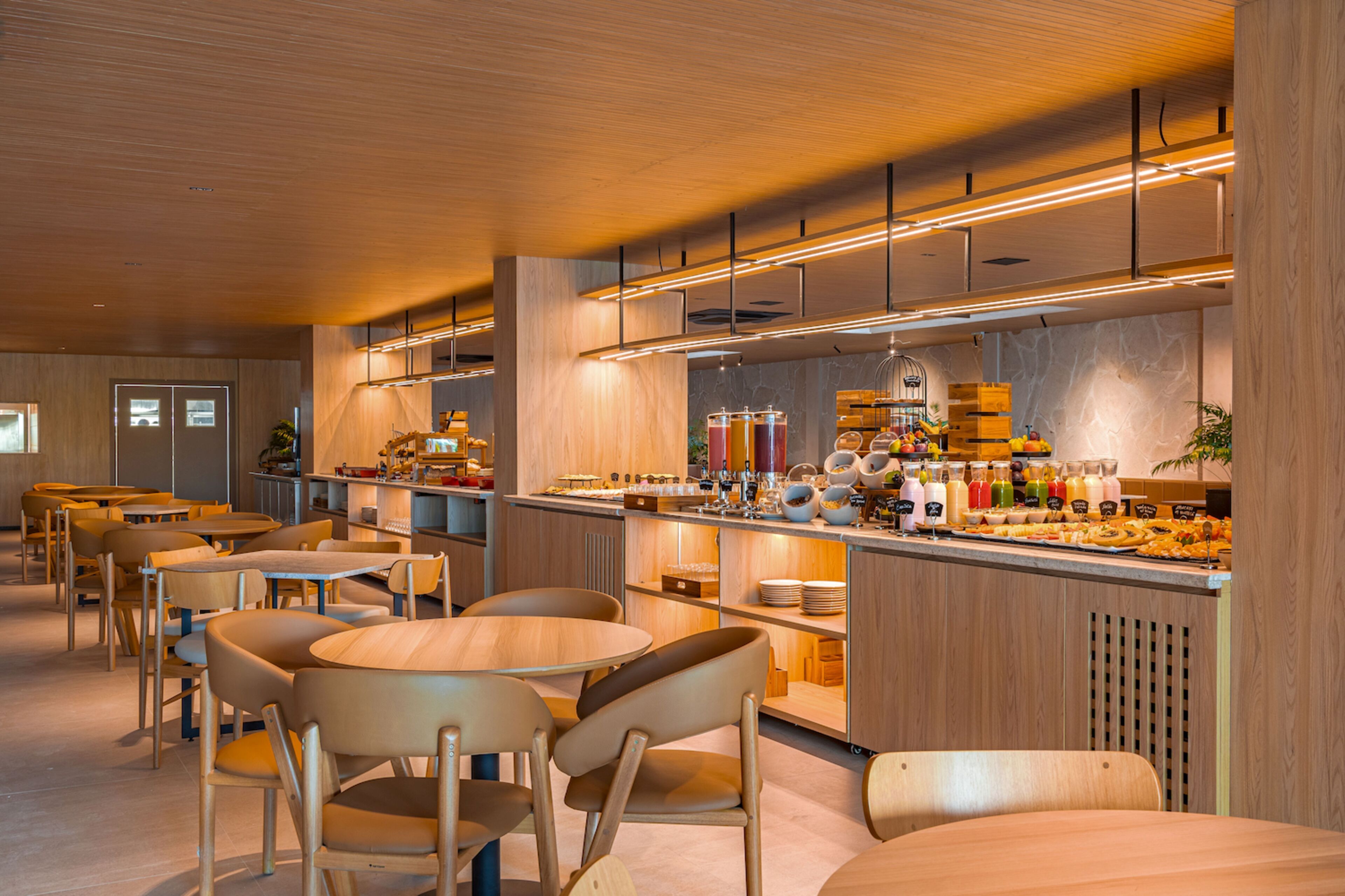 A modern cafe interior with wooden furniture, a central counter with a variety of food and drink options, and a clean, well-lit atmosphere.