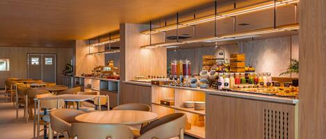 A modern cafe interior with wooden furniture, a central counter with a variety of food and drink options, and a clean, well-lit atmosphere.