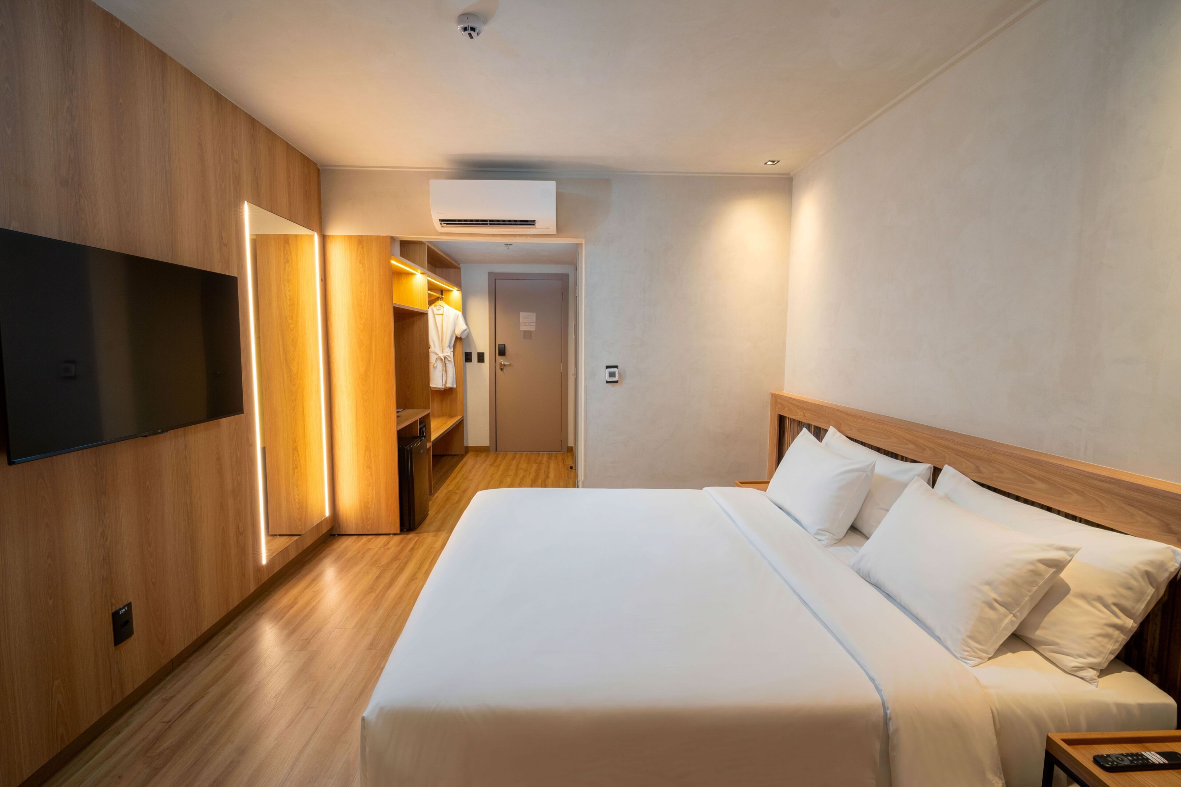 Ein Hotelzimmer mit einem großen Bett, einem an der Wand montierten Fernseher, einem Kleiderschrank und einer Klimaanlage.