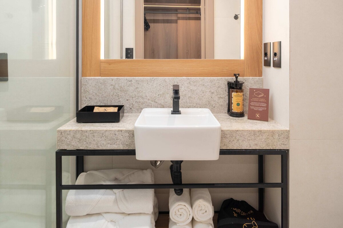 A modern bathroom with a large mirror, a white sink, and a shelf with towels.