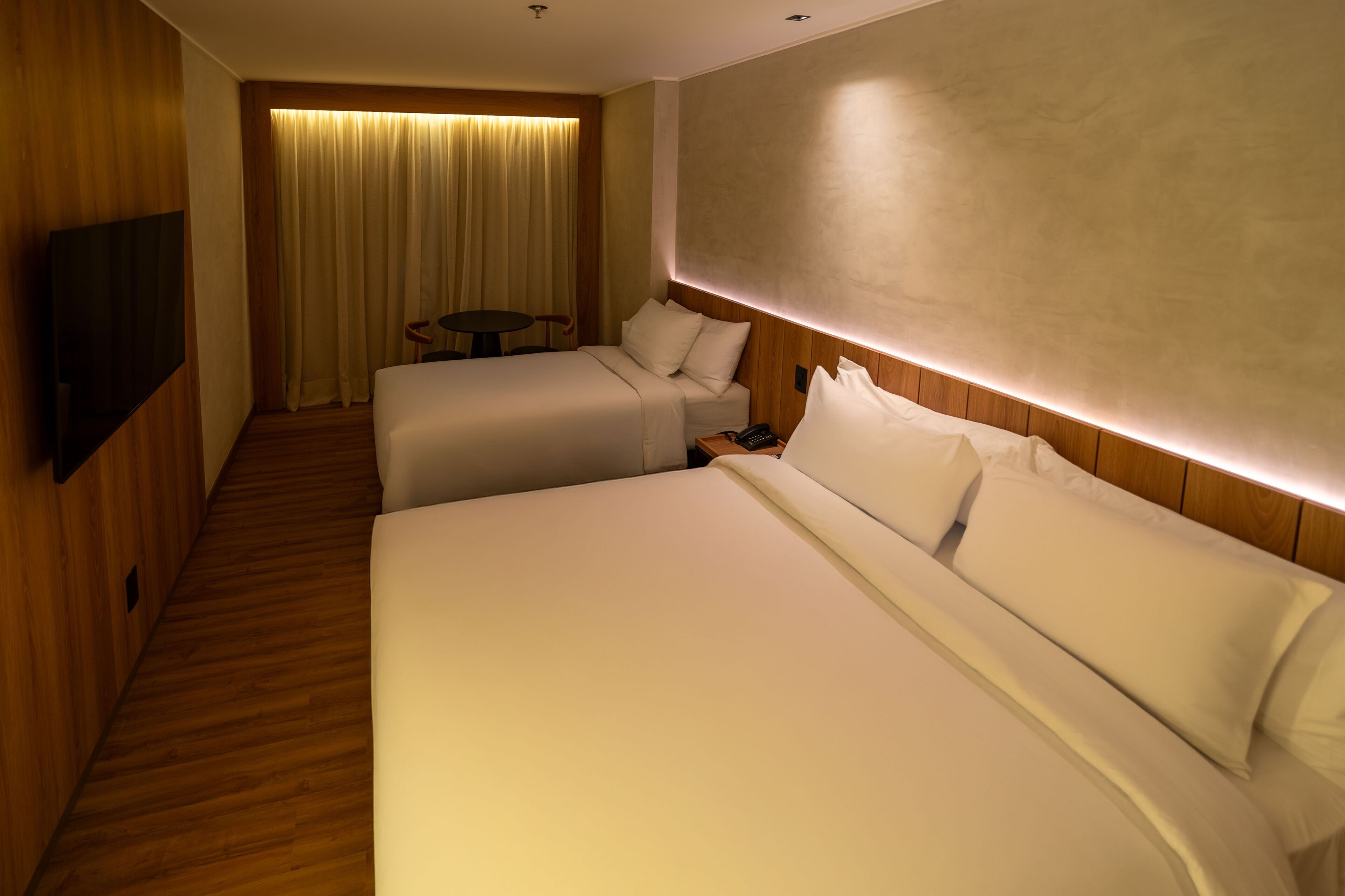 Habitación de hotel con dos camas, un televisor, una mesita y una cortina.