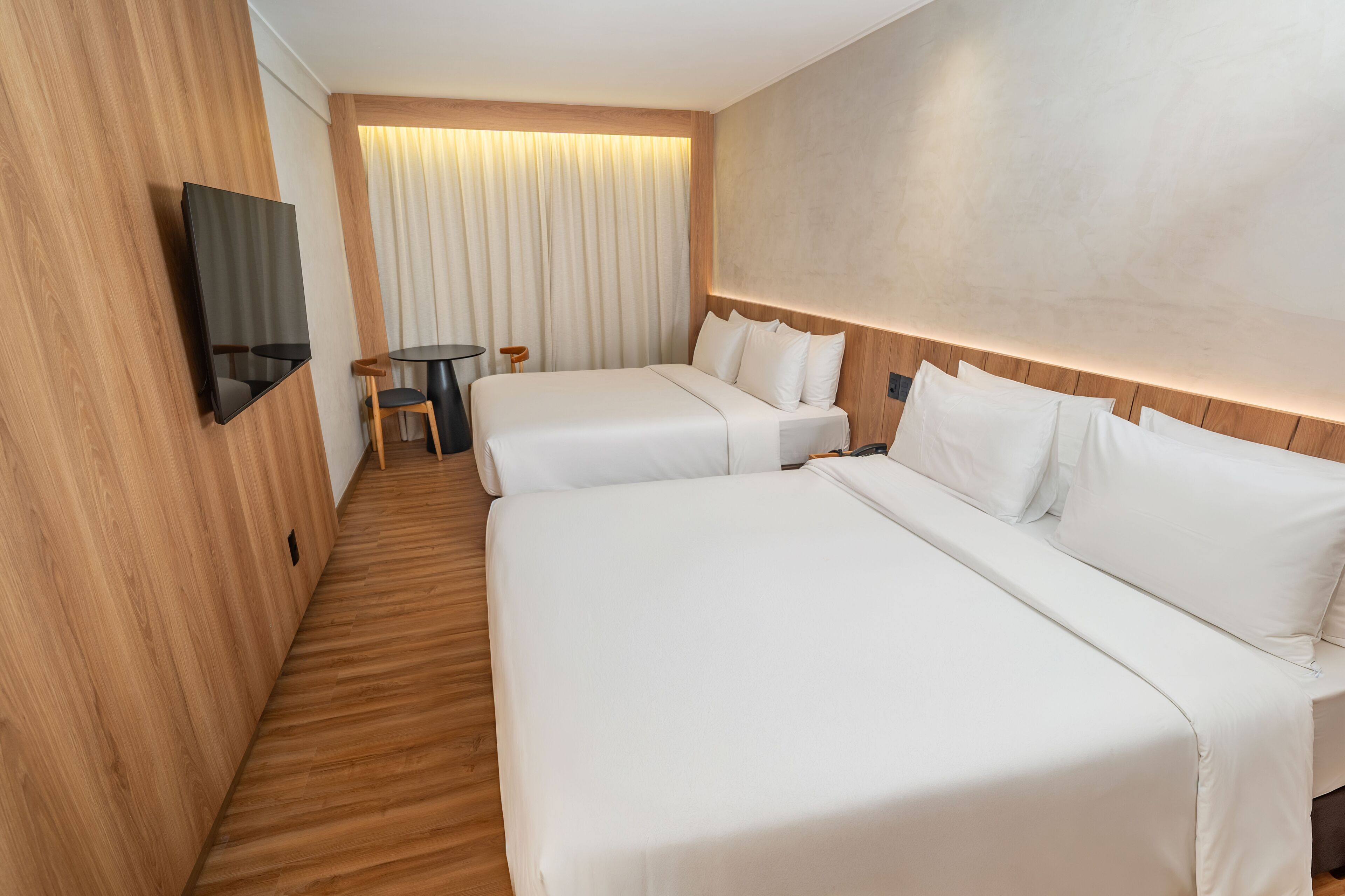 Une chambre d’hôtel avec deux lits, un téléviseur fixé au mur, une petite table et un rideau.