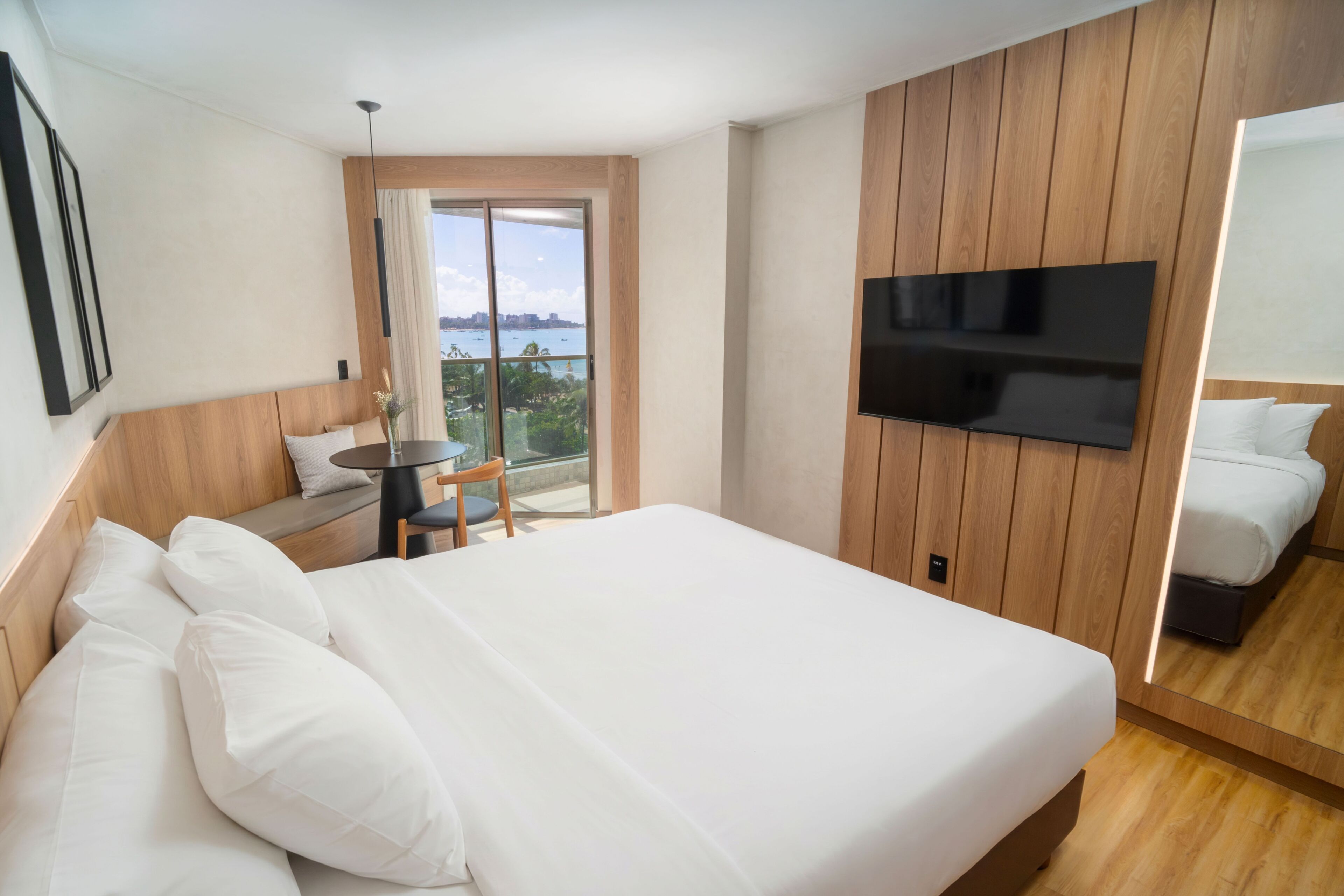 Habitación de hotel con una cama grande, un televisor montado en la pared, un balcón con vistas y una mesita con una silla.