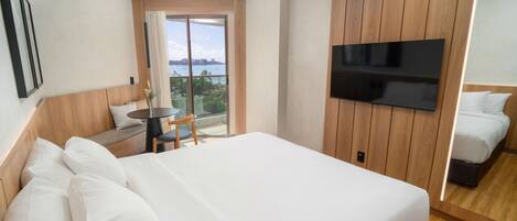 Habitación de hotel con una cama grande, un televisor montado en la pared, un balcón con vistas y una mesita con una silla.
