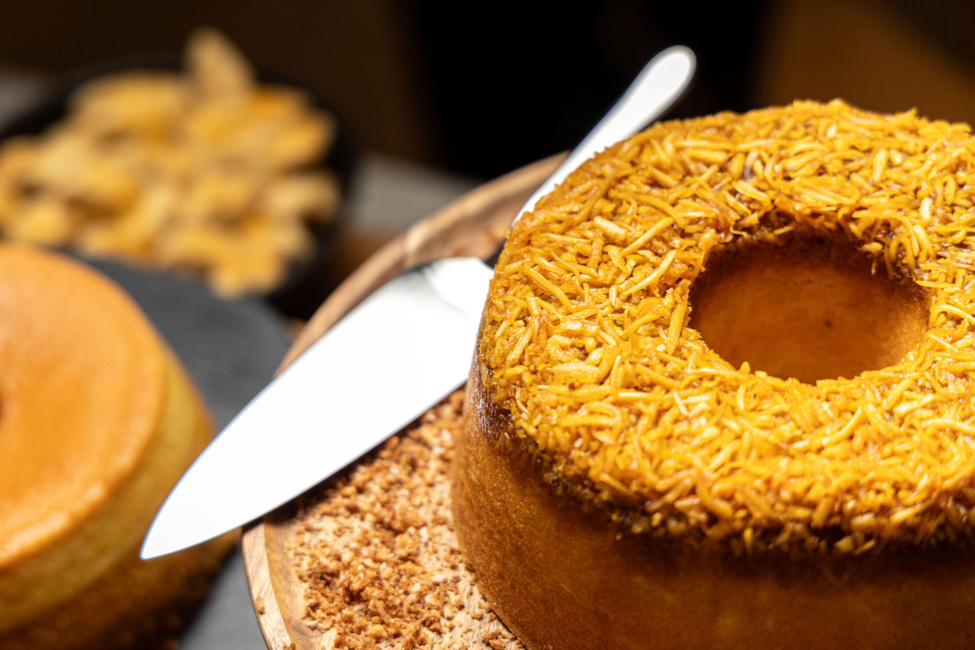 A close-up of a donut with a hole in the center, covered in a golden, crispy topping, and a knife beside it.