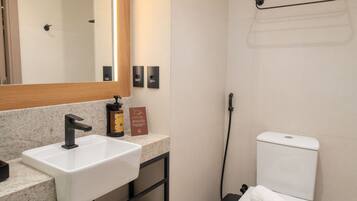 A modern bathroom with a white sink, black faucet, and a toilet. There is a towel rack on the wall and a shelf with folded towels.