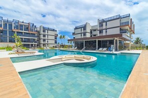 A modern hotel with a swimming pool, lounge chairs, and a covered area. - Cais Eco Residência By Carpediem (Ipojuca)
