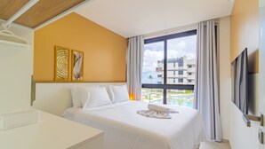 A hotel room with a bed, a desk, a TV, and a window with a view of a building and a pool.