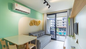 A modern living room with a sofa, a dining table, chairs, a TV, and a balcony with a pool view.