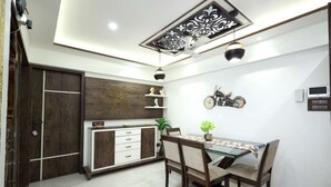 A dining area with a glass table, wooden chairs, a decorative ceiling, and a wall-mounted clock. - 2 Bedroom Apartments (Mumbai)