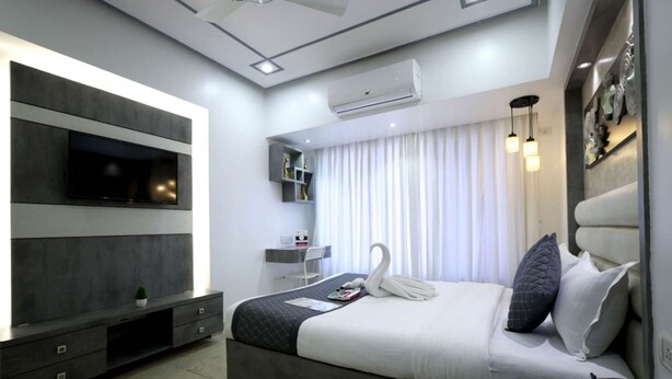 A modern hotel room with a large bed, a TV mounted on the wall, a desk, and a window with curtains. - 2 Bedroom Apartments (Mumbai)