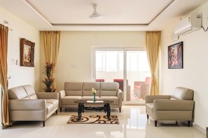 A living room with a beige sofa set, a round coffee table, and a large window with curtains. - Euphoria Penthouse (Hyderabad)