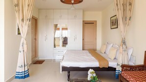 Ein Schlafzimmer mit einem Bett, einem Holzstuhl, einem Nachttisch, einem Kleiderschrank und einem Deckenventilator.
