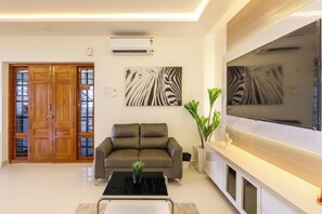 Ein modernes Wohnzimmer mit einer Couch, einem Couchtisch mit Pflanze, einem flachbildfernseher an der Wand und einer Holztür mit Glasfeldern.