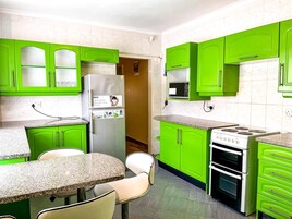 Una cocina con gabinetes verdes, un refrigerador, un microondas, una estufa y un comedor con una mesa y sillas.