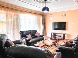 Un salón con sofás de cuero, una mesa de centro de vidrio y un televisor de pantalla plana en la pared.