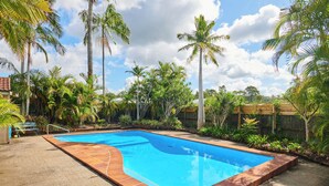 Ein rechteckiger Swimmingpool mit Fliesenbordstein, umgeben von Palmen und einem Holzzaun.