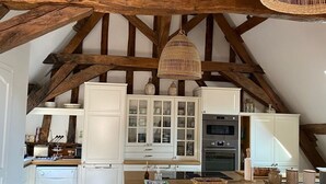 Una cucina con mobili bianchi, soffitto in legno e lampadario in vimini.