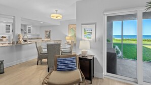 A modern kitchen with white cabinets, a dining area with wicker chairs, and a view of the ocean through a large sliding glass door. - Gulf-Front Grandeur in Longboat Key – Luxurious & Spacious Condo #102 by RVA (Longboat Key)