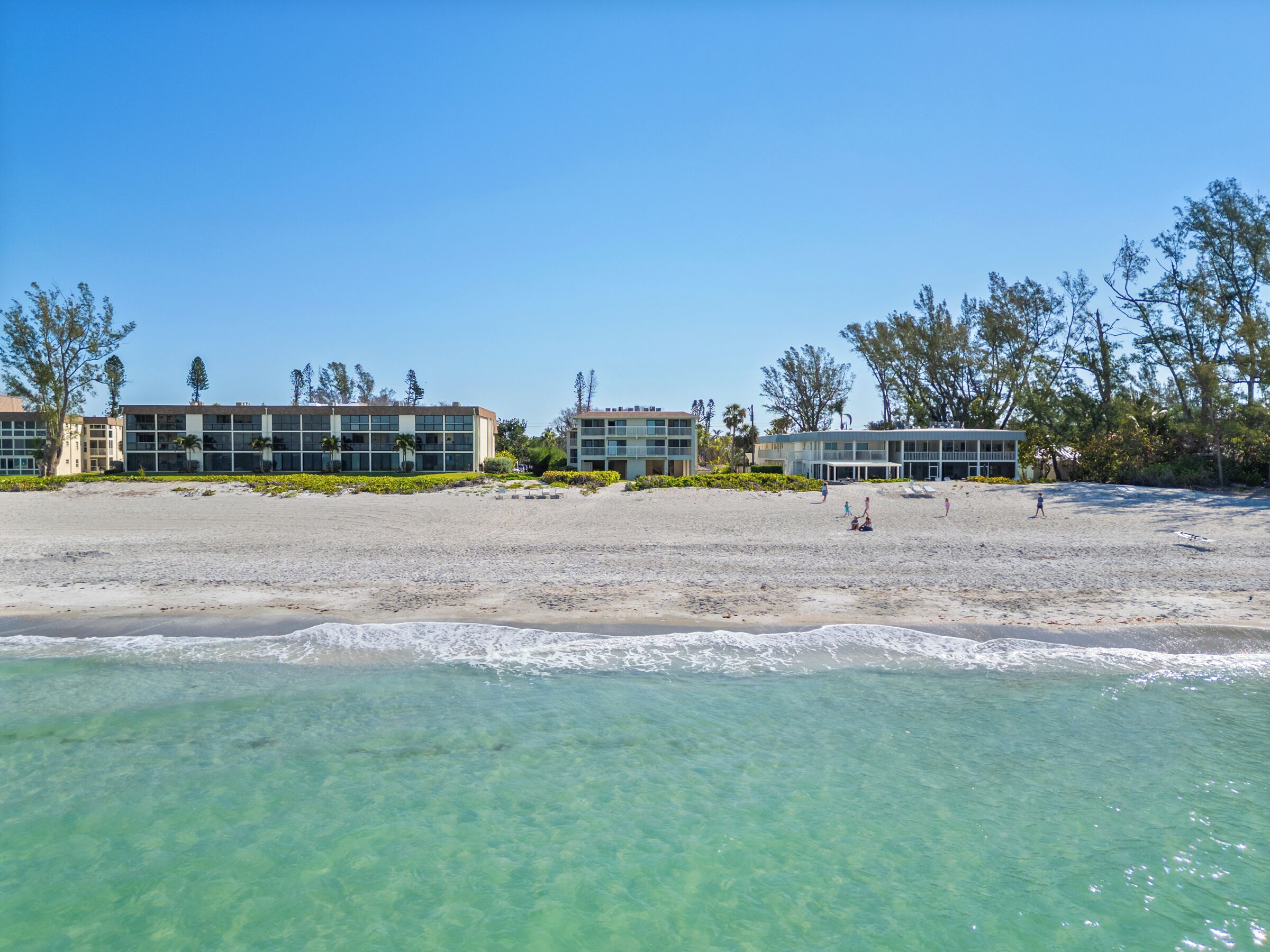 Un hôtel situé en bord de mer, composé de plusieurs bâtiments, avec une eau turquoise cristalline et une plage de sable.