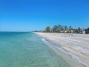 Ein Strand mit klarem türkisblauem Wasser, einem sandigen Ufer und einer Reihe von Gebäuden mit freiem Blick auf den Ozean.