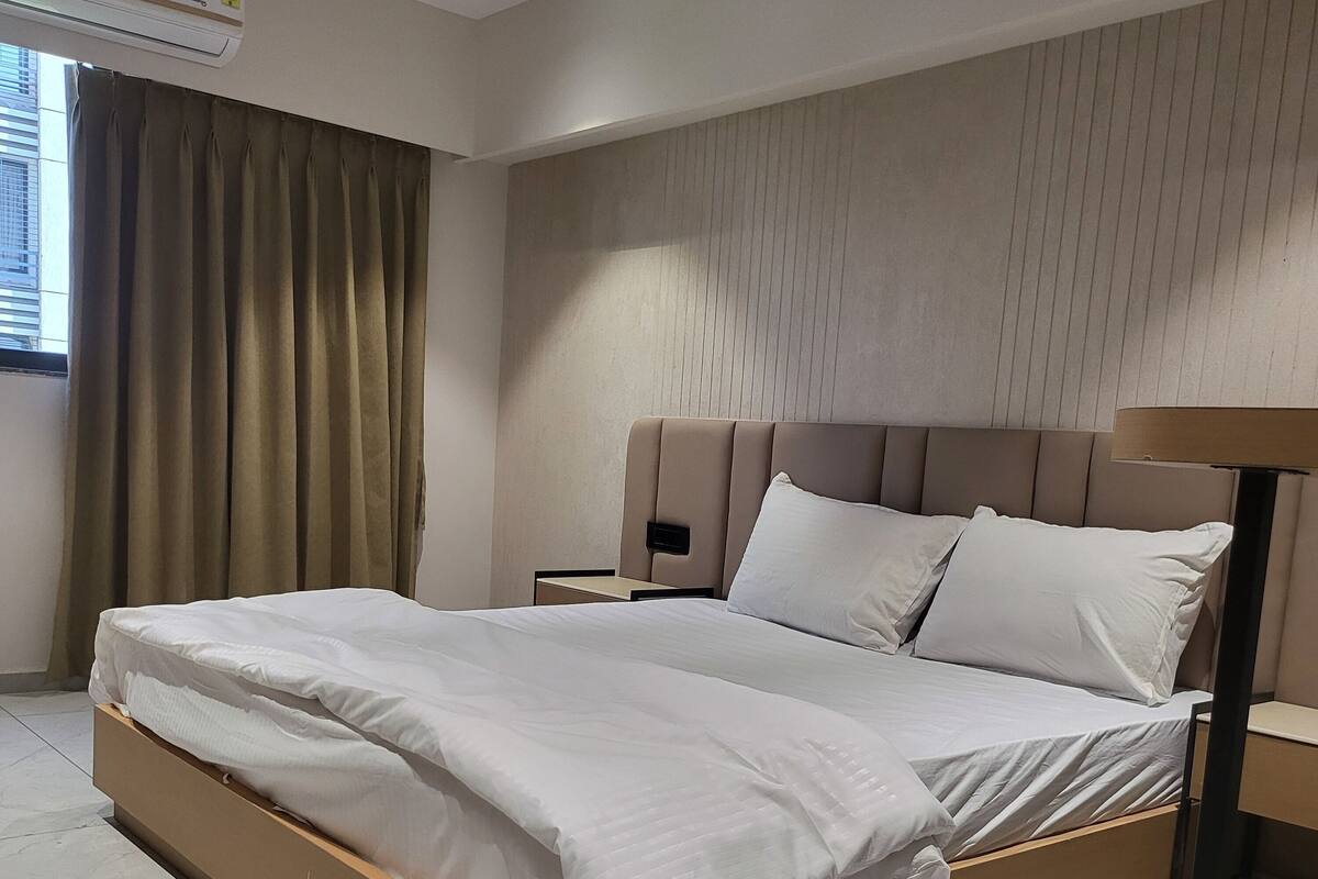 A modern bedroom with a large bed, a nightstand, a lamp, and a window with curtains.