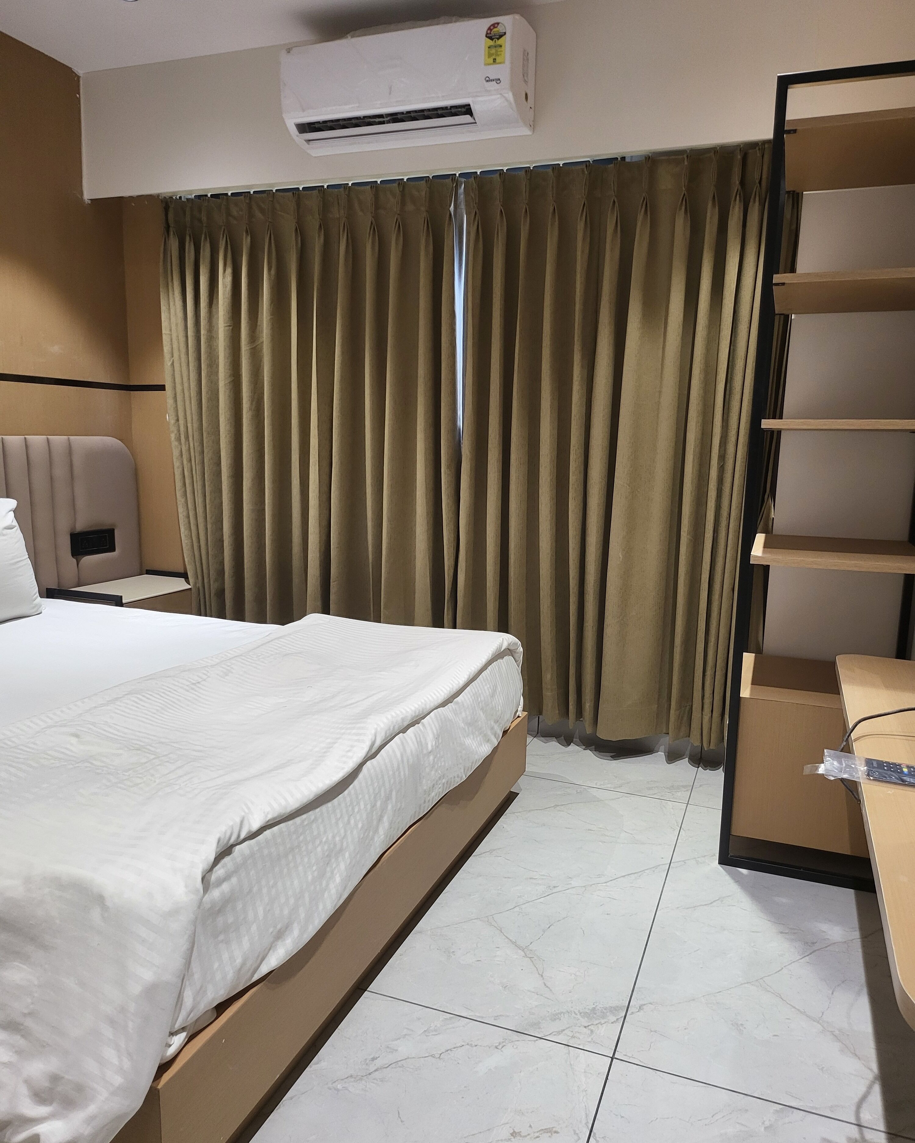A hotel room with a bed, a desk, a chair, a wardrobe, and an air conditioning unit.