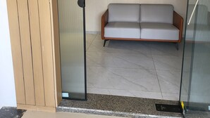 A modern room with a glass partition, a grey sofa, and a ceiling fan. - Hotel Shiv Kartik (Surat)