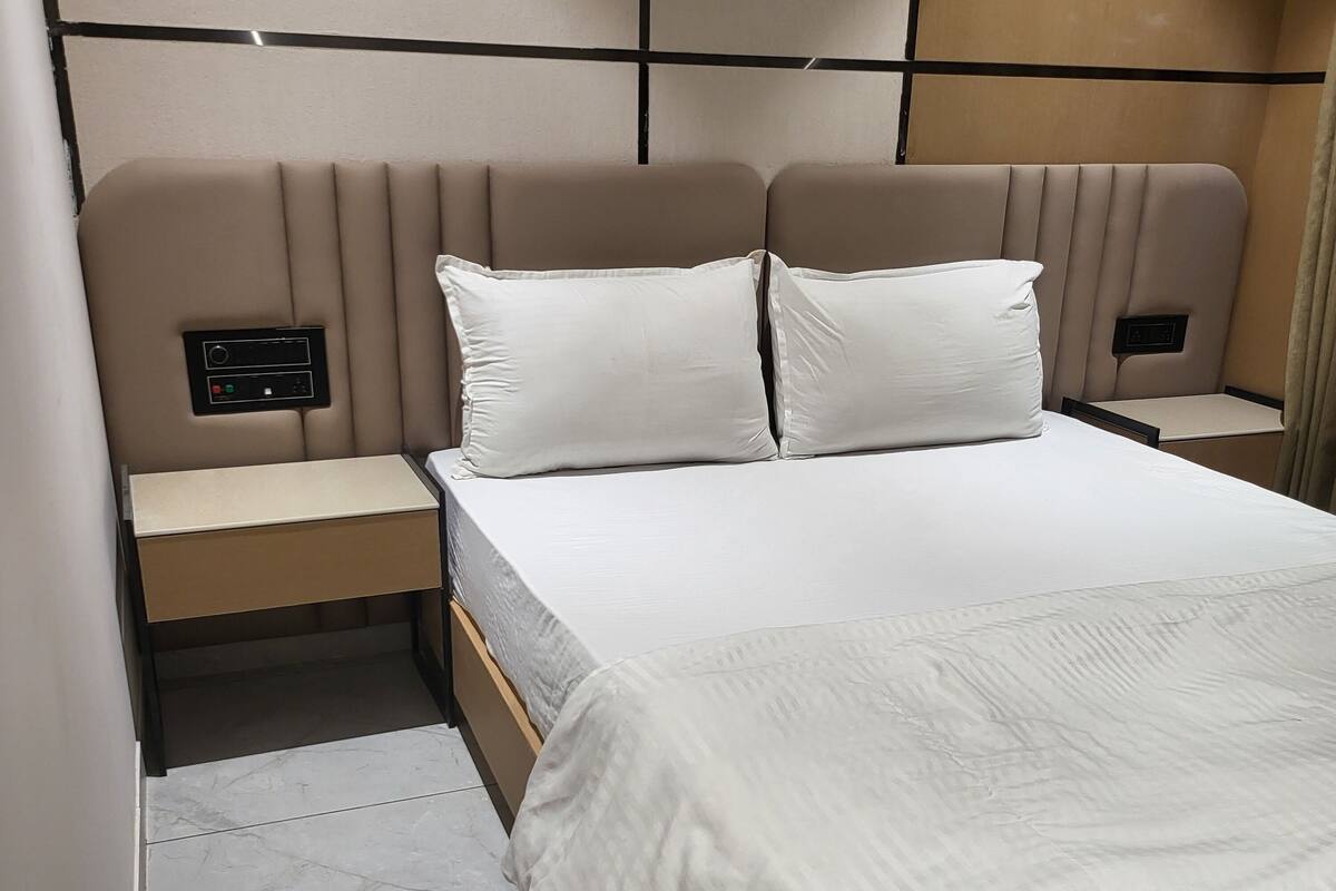 A modern hotel room with a large bed, two bedside tables, and a control panel on the headboard.