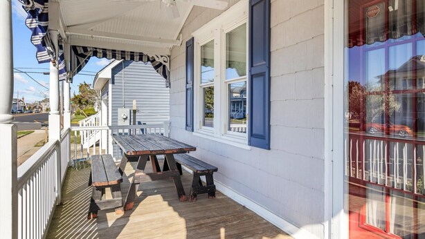Eine Veranda mit Holzbank und Tisch, weiß verkleidet und mit blauen Fensterläden.