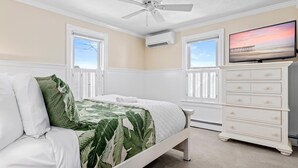 Ein Schlafzimmer mit Bett, Kommode, Fernseher und zwei Fenstern mit Rollläden.