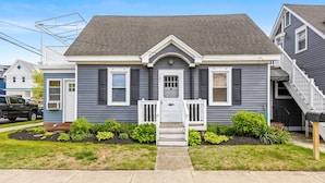 A two-story house with a front porch, a mailbox, and a driveway with a lawn. - 3BR Charming Beach Cottage | North End OC (Ocean City)