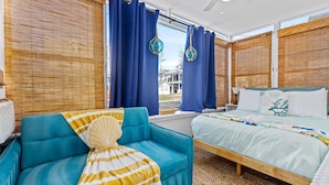 A modern hotel room with a bed, a blue sofa, and a view of the outside. - 3BR Charming Beach Cottage | North End OC (Ocean City)