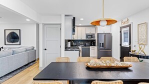 A modern kitchen with white cabinets, a black refrigerator, and a dining area with a black table and wicker chairs. - 3BR Modern 2nd Floor Condo | Easy Walk to Beach! (Ocean City)