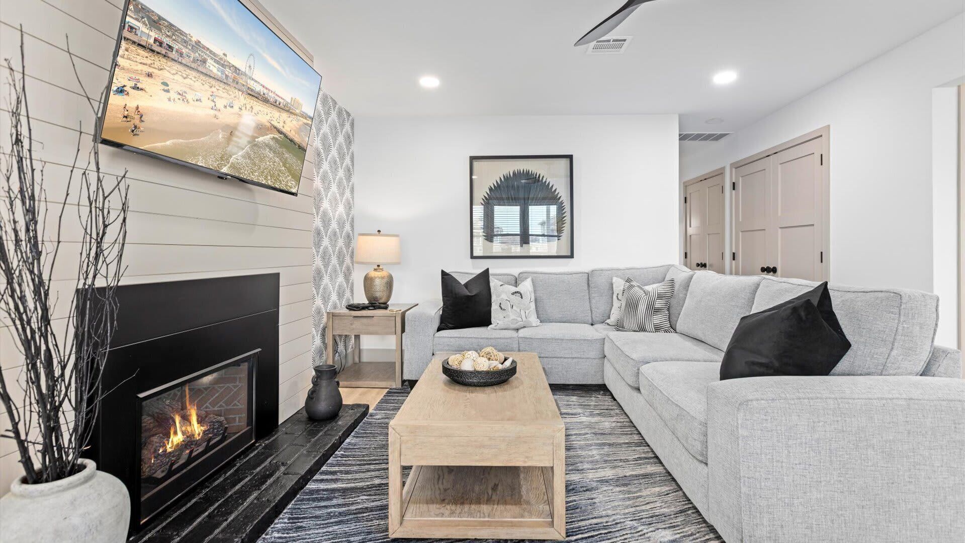 A modern living room with a fireplace, a grey sofa, a coffee table, and a TV displaying a beach scene.