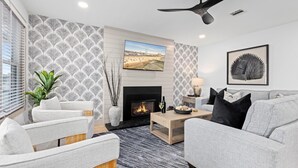A modern living room with a fireplace, a sofa, a coffee table, and a TV mounted on the wall. - 3BR Modern 2nd Floor Condo | Easy Walk to Beach! (Ocean City)
