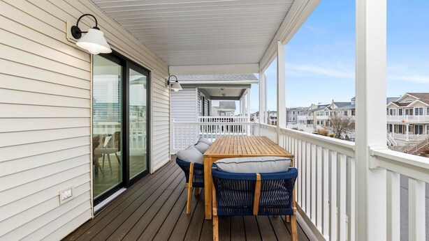 A covered outdoor deck with a wooden table and blue wicker chairs, overlooking a residential area. - 3BR Modern 2nd Floor Condo | Easy Walk to Beach! (Ocean City)