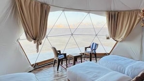 Acomodação em tenda com duas camas, uma mesinha, cadeiras e vista para o mar.