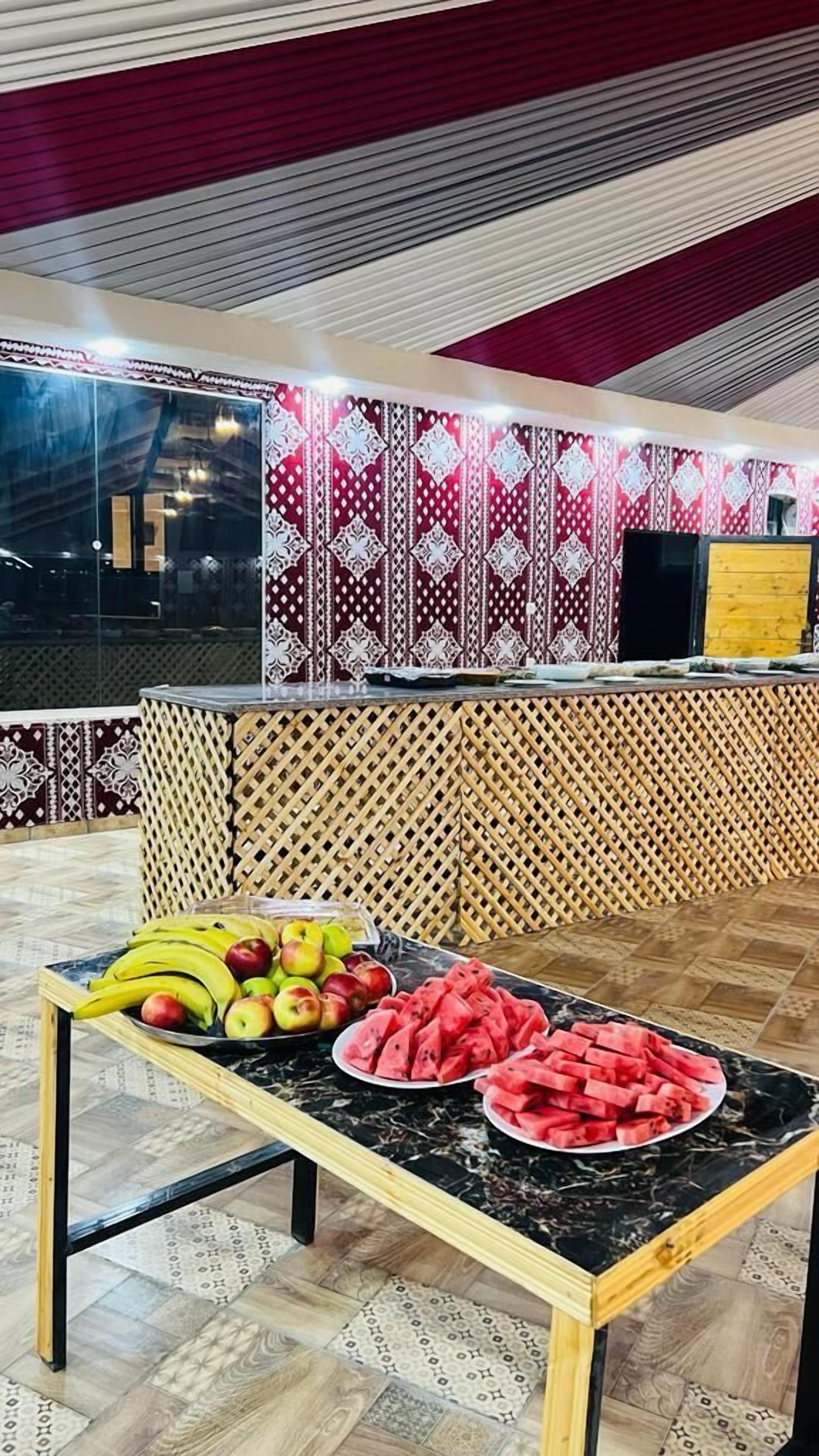 A kitchen area with a marble countertop displaying fruits, a patterned wall, and a wooden lattice partition.