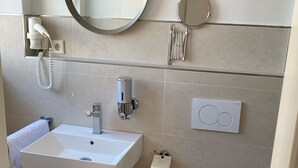 A modern bathroom with a white sink, mirror, toilet, and a trash bin. - Erde Hotel Erlangen (Erlangen)