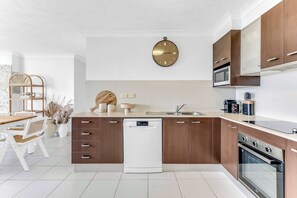 Une cuisine moderne avec des meubles en bois, un lave-vaisselle, un four à micro-ondes et une horloge au mur.