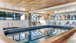 An indoor swimming pool with clear glass walls, lounge chairs, and a wooden ceiling. - Tiki by Khove (Surfers Paradise)