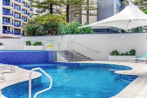 A swimming pool with blue mosaic tiles, a white canopy, and a staircase leading to an upper level.