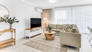 A modern living room with a sofa, TV, and decorative plants. - Tiki by Khove (Surfers Paradise)