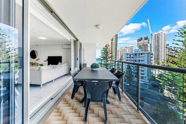 A modern balcony with a dining table and chairs, a sofa, and a TV.