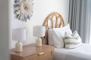 A neatly made bed with white and striped pillows, a wooden nightstand with two white lamps, and a decorative wall piece.