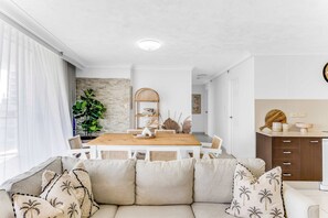 A modern living room with a beige sofa, a wooden dining table, and a kitchen area with a wooden cabinet.