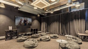 Una sala de cine moderna con asientos tipo sillón de mimbre, una pantalla grande y un telón oscuro de fondo.