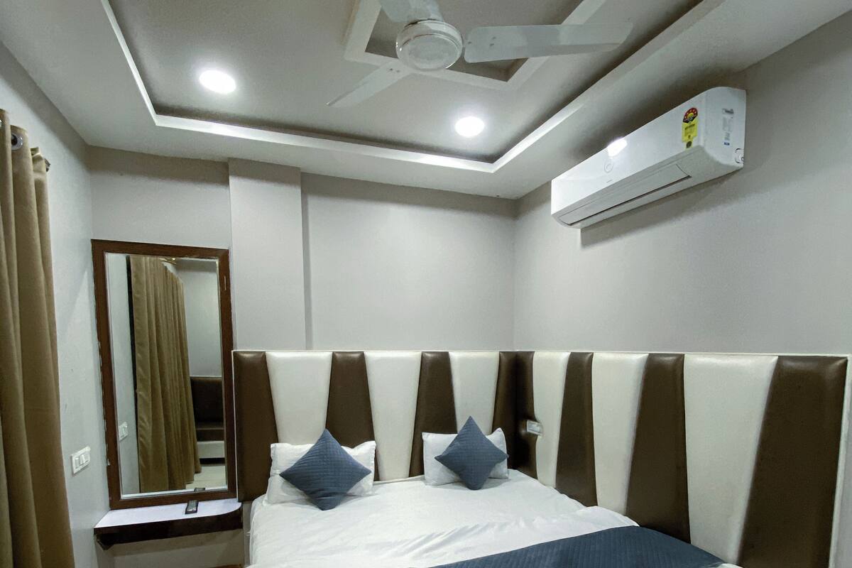 Une chambre d’hôtel équipée d’un lit, d’un ventilateur de plafond, d’un appareil de climatisation, d’un miroir et d’une fenêtre avec des rideaux.
