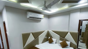 A modern hotel room with a large bed, a ceiling fan, an air conditioning unit, and a mirror on the wall. - Hotel Pleasure (Ujjain)